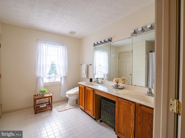 full bathroom featuring toilet, a textured ceiling, double vanity, and a sink