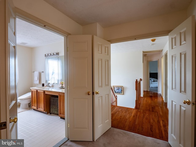 hallway featuring a sink, a textured ceiling, and an upstairs landing