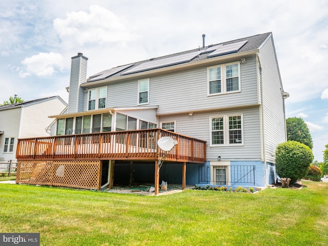 rear view of property with a yard, a chimney, a sunroom, roof mounted solar panels, and a deck