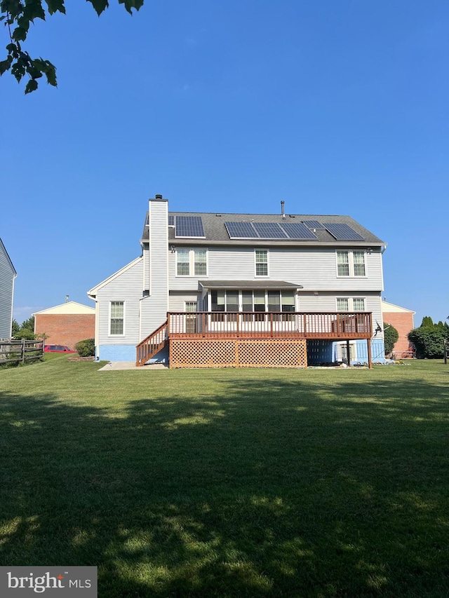 back of house featuring solar panels, a yard, a chimney, and a wooden deck