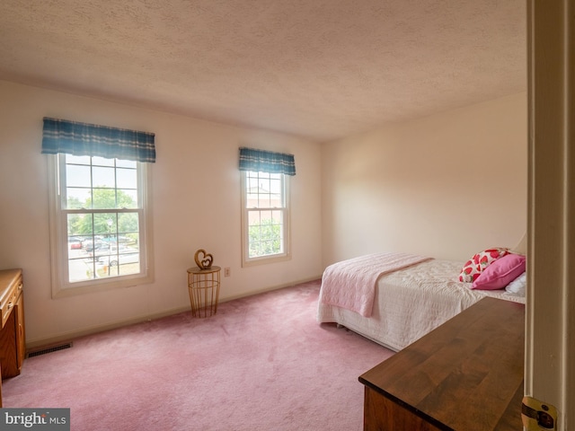 bedroom featuring light carpet, a textured ceiling, visible vents, and baseboards