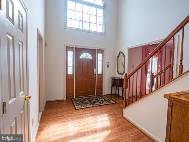 foyer with stairs, light wood finished floors, and a high ceiling