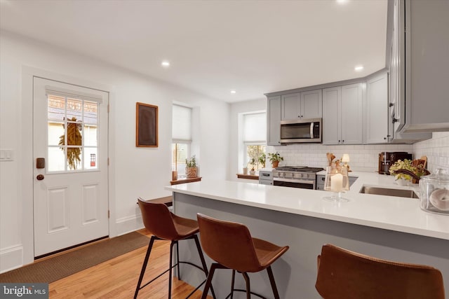 kitchen with appliances with stainless steel finishes, backsplash, a peninsula, and gray cabinetry