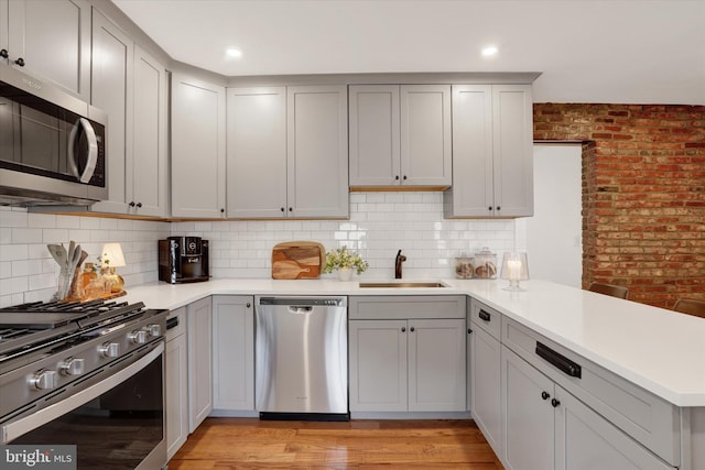 kitchen with a peninsula, gray cabinets, stainless steel appliances, and a sink