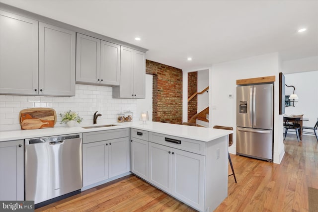 kitchen with appliances with stainless steel finishes, a sink, a peninsula, and gray cabinetry