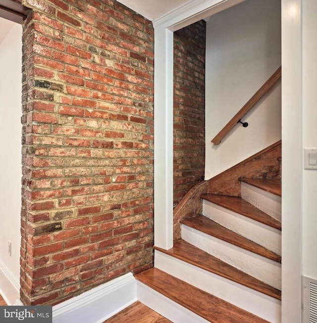 stairway featuring brick wall, wood finished floors, and baseboards