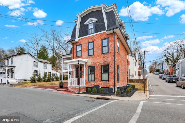 view of front of property featuring a residential view, brick siding, roof with shingles, and mansard roof