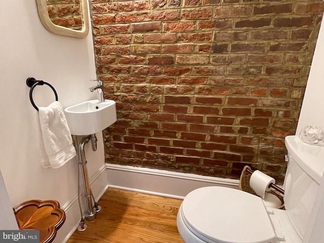 bathroom with brick wall, wood finished floors, and toilet