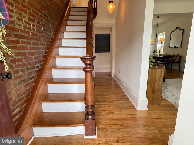 staircase featuring brick wall, baseboards, and wood finished floors