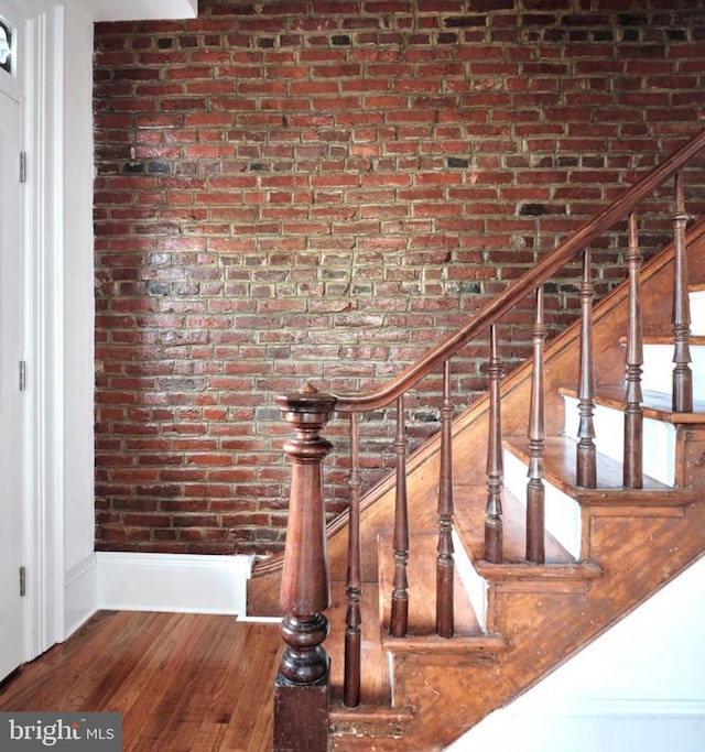 stairs featuring brick wall and wood finished floors