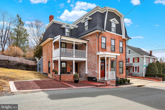 victorian home with mansard roof, roof with shingles, fence, and brick siding