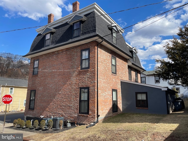 view of side of property with a shingled roof, brick siding, a chimney, and mansard roof