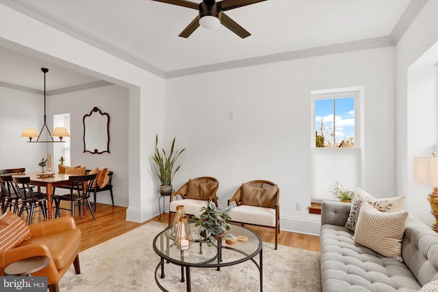 living area featuring light wood-style floors, baseboards, crown molding, and ceiling fan with notable chandelier