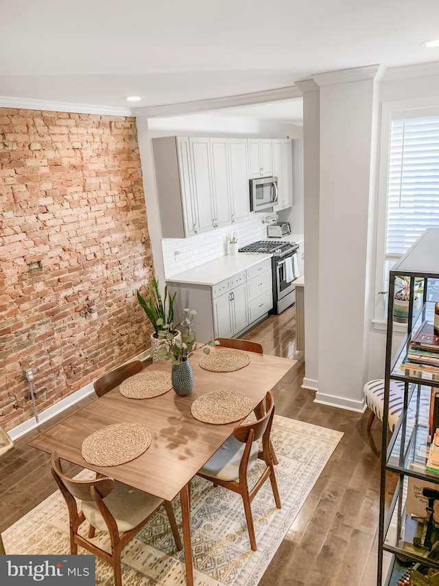 dining room featuring dark wood-style floors, baseboards, brick wall, and crown molding