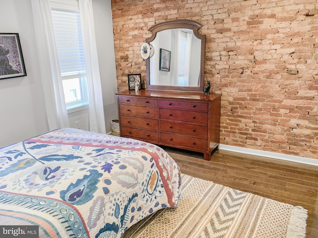 bedroom with wood finished floors, baseboards, and brick wall