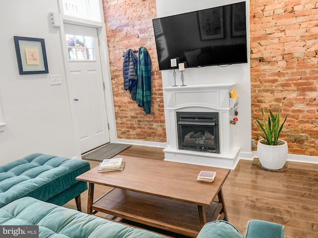 living room with wood finished floors, a fireplace with raised hearth, baseboards, and brick wall