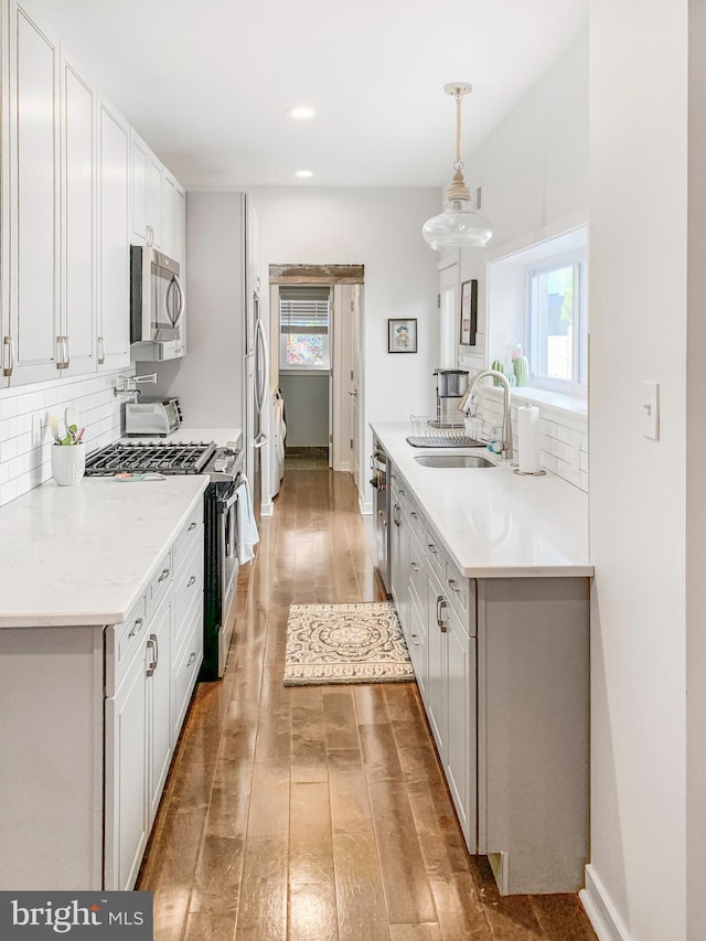 kitchen with light wood finished floors, plenty of natural light, stainless steel appliances, a sink, and tasteful backsplash