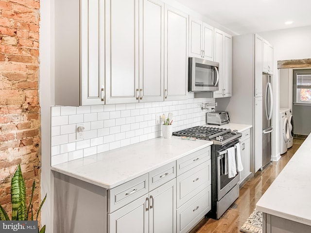 kitchen with light wood-type flooring, light stone counters, washer / clothes dryer, stainless steel appliances, and decorative backsplash