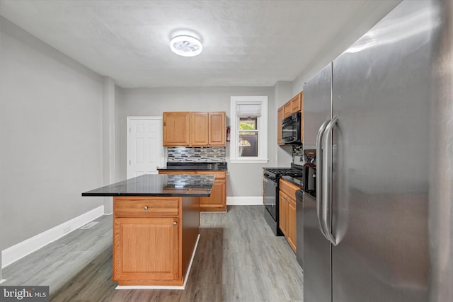 kitchen featuring a center island, dark countertops, decorative backsplash, wood finished floors, and black appliances