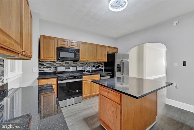 kitchen with arched walkways, light wood-style flooring, stainless steel appliances, a sink, and tasteful backsplash