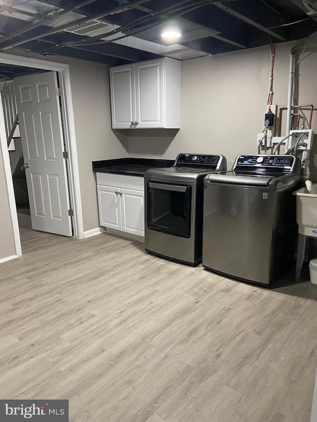 washroom with baseboards, light wood-type flooring, cabinet space, and washer and dryer