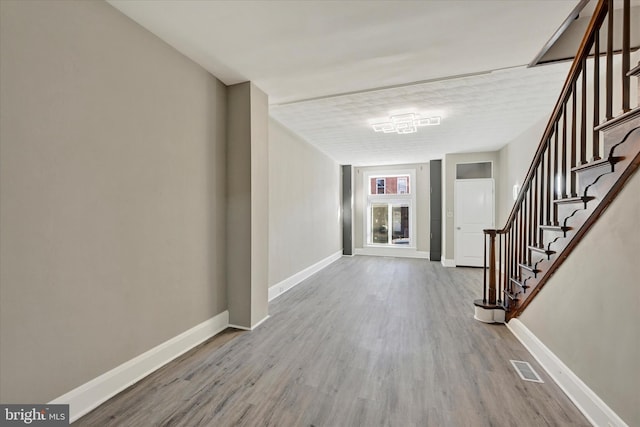 foyer entrance featuring stairway, visible vents, baseboards, and wood finished floors