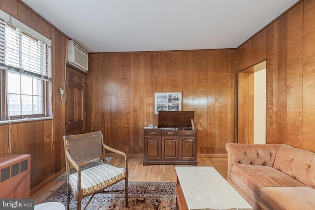 sitting room featuring radiator heating unit, a wall mounted air conditioner, light wood-style flooring, and wooden walls