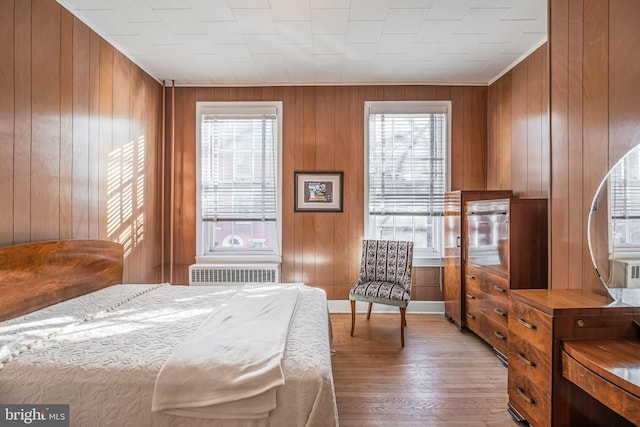 bedroom featuring radiator heating unit, wood walls, multiple windows, and light wood-style flooring