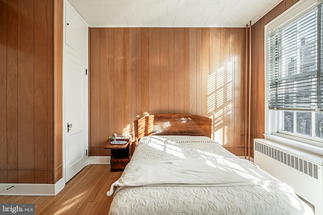 bedroom with radiator heating unit, wooden walls, baseboards, and wood finished floors