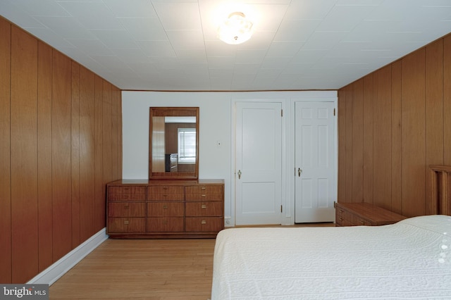 bedroom with a closet, baseboards, wood walls, and light wood finished floors