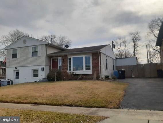 tri-level home with driveway, brick siding, a front lawn, and fence