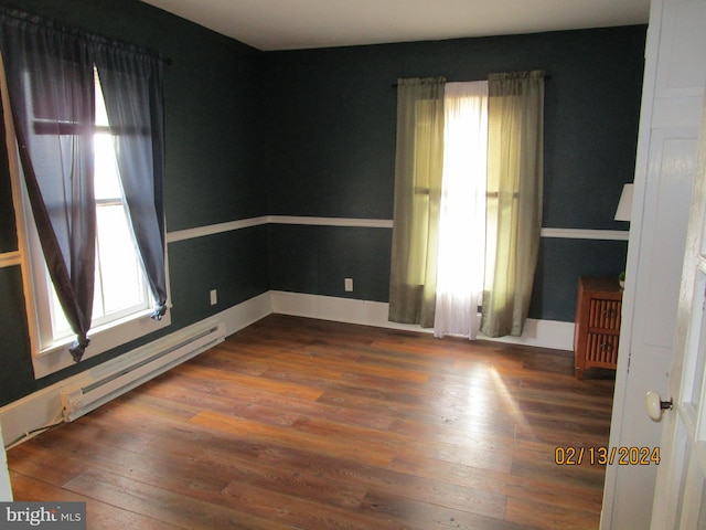 unfurnished room featuring baseboard heating, wood finished floors, and a wealth of natural light