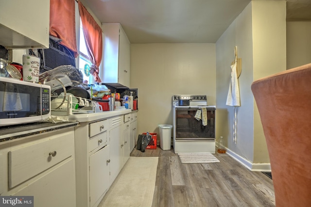 kitchen with baseboards, range with electric cooktop, white cabinets, white microwave, and light wood-type flooring