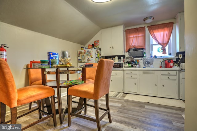 kitchen featuring vaulted ceiling, light wood-type flooring, freestanding refrigerator, and white cabinets