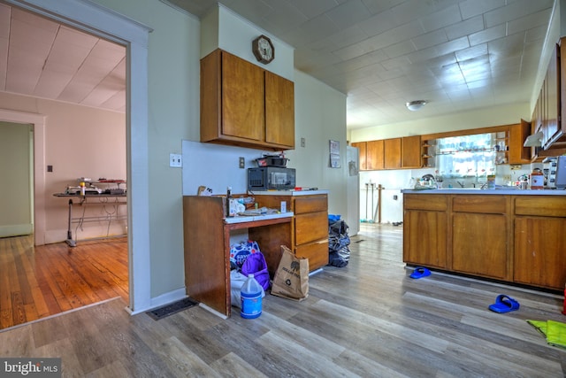 kitchen with black microwave, wood finished floors, baseboards, light countertops, and brown cabinetry