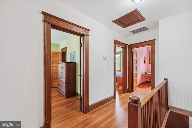 hall featuring light wood-style floors, attic access, visible vents, and baseboards