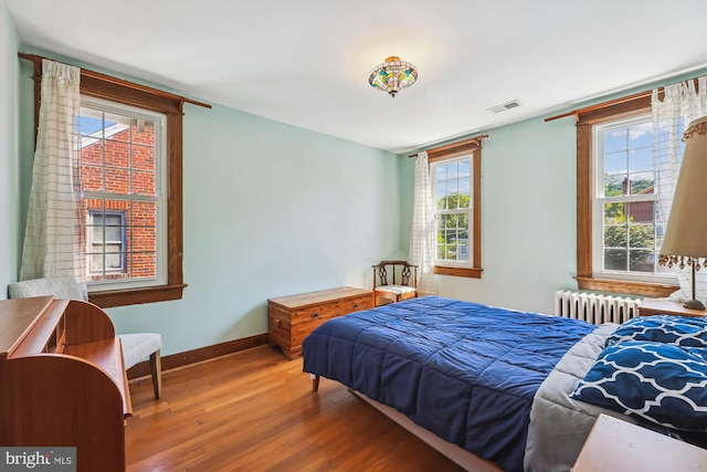 bedroom with radiator, baseboards, visible vents, and wood finished floors