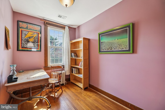 home office with radiator heating unit, wood-type flooring, visible vents, and baseboards