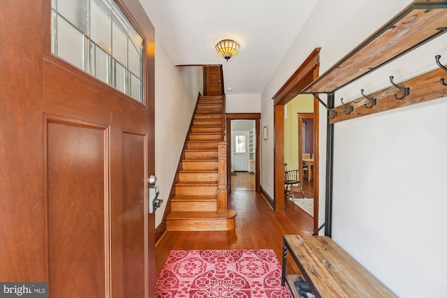 foyer entrance featuring baseboards, stairway, and wood finished floors