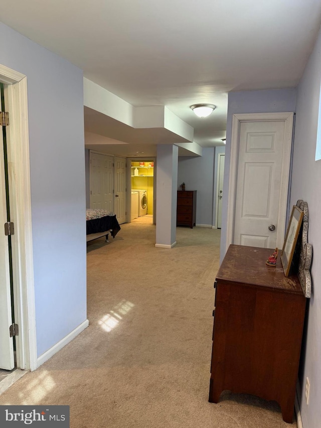 corridor with baseboards, light colored carpet, and washing machine and clothes dryer