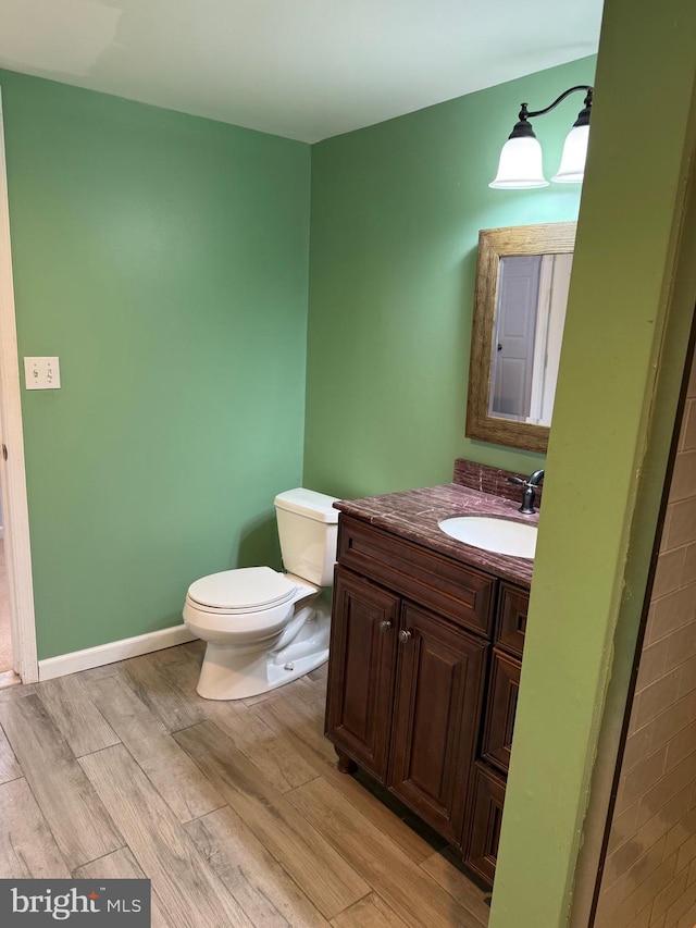 bathroom featuring toilet, baseboards, wood finished floors, and vanity