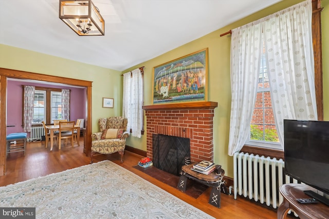 sitting room with radiator heating unit, a brick fireplace, and wood finished floors