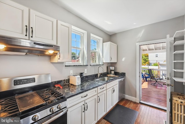 kitchen with white cabinets, hardwood / wood-style flooring, appliances with stainless steel finishes, under cabinet range hood, and a sink