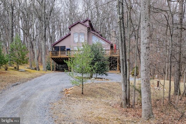 rustic home with a forest view, a wooden deck, and driveway