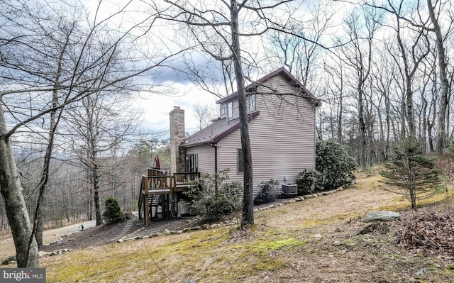 view of side of property featuring cooling unit, a wooden deck, a chimney, and stairway