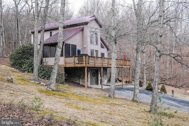 exterior space featuring a deck, driveway, a standing seam roof, metal roof, and a carport