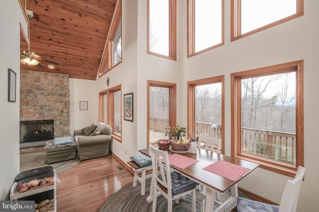 dining area with wood finished floors, a fireplace, ceiling fan, wood ceiling, and a towering ceiling