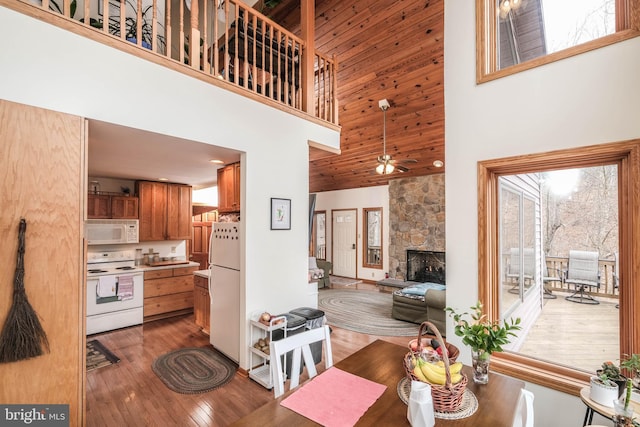 kitchen featuring hardwood / wood-style floors, white appliances, brown cabinetry, a fireplace, and a towering ceiling