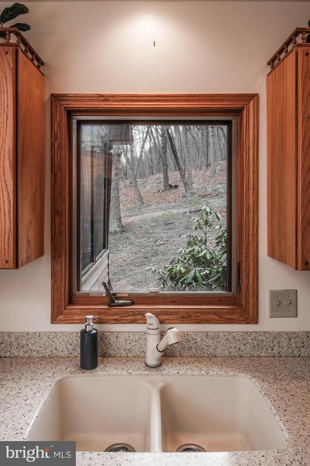 interior details featuring brown cabinetry, light stone counters, and a sink