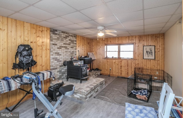 interior space featuring wooden walls, a paneled ceiling, a ceiling fan, and a wood stove